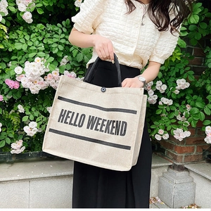 Close-up of Hello Weekend linen tote bag with button closure and black woven handles
