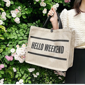 Detail of linen tote bag featuring HELLO WEEKEND print and black woven handles