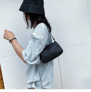 Detail of black woven shoulder bag with leather strap and silver metal chain accessory