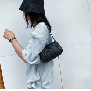 Minimalist black woven shoulder bag with chain strap shown on model in a modern style