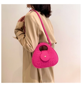 Détail du sac selle fuchsia avec texture crocodile porté sur un trench-coat beige