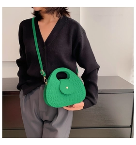 Détail d'un sac sous le bras en feutre vert à motif crocodile et fermoir doré