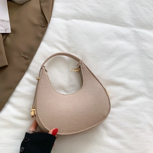 Chic beige half-moon hobo bag with gold hardware being held against a casual blazer
