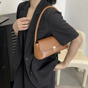 Detail of a dark brown faux leather baguette bag featuring a gold metal push-lock closure