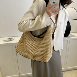 Sac hobo en paille tressée beige avec anses en cuir noir porté par un mannequin