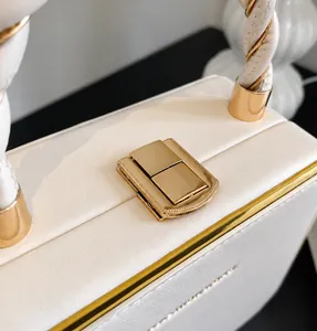 Detail of golden square metal lock and white leather texture on a box-style handbag