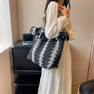 Handwoven geometric tote bag with black and white tassels and brown leather handles