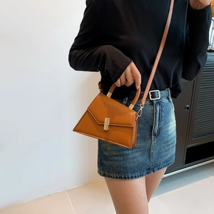 Sac trapèze minimaliste en cuir marron avec boucle dorée et poignée porté par un modèle