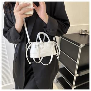 Close-up of a white mini shell bag with glossy leather, top handles and shoulder strap