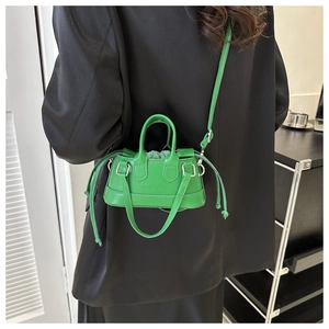 Mini bright green shell bag worn crossbody over a black blazer showing glossy texture