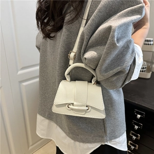 Detail of white lychee leather texture and cross-belt buckle on trapezoid small bag