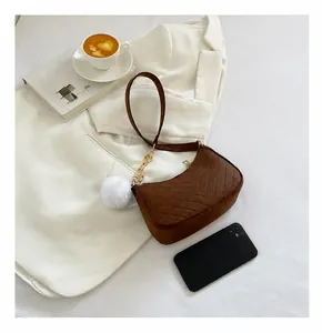 Detail of a brown suede crossbody bag with V-shaped quilting and a white fur pompom charm