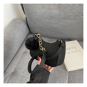 Close-up of black quilted crescent bag with gold chain strap and faux fur pompom detail