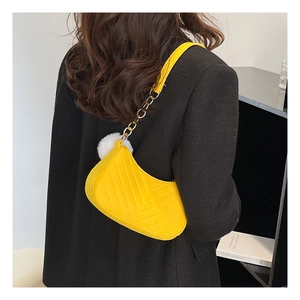 Detail of yellow quilted crossbody bag with gold chain strap and fluffy pompom charm