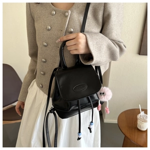 Detail of black matte leather backpack with drawstring closure and pink plush charm accessory