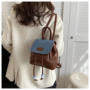 Detail of a mini backpack featuring denim and brown leather patchwork with colorful beads