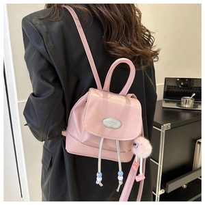Close-up of pink glossy mini backpack with metal logo and fluffy ball charm accessory