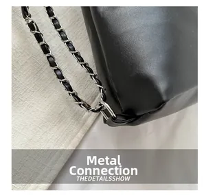 Detail of silver chain strap connected to black leather bag with precise stitching