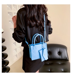 Detail of light blue textured felt tote bag with detachable pouch on a leather chair