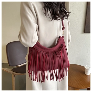 Detailed back view of a burgundy leather shoulder bag with long fringes on a beige trench coat
