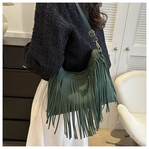 Model showing dark green crescent shoulder bag with dense fringe tassels and adjustable strap
