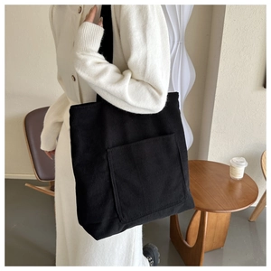 Detail shot of large black corduroy tote bag showing its ribbed texture and front pocket