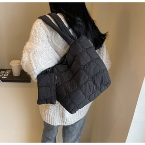 Detailed view of black quilted puffer tote bag with matching zipper pouch worn on shoulder