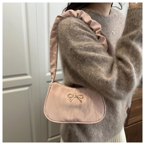 Detail of light pink pleated shoulder bag with golden bow ornament on a woman