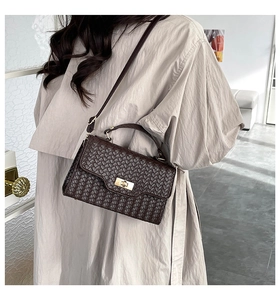 Detailed view of dark brown woven texture handbag with golden twist lock on a shoulder strap