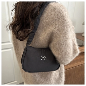 Détail du sac croissant noir avec nœud argenté porté sur un pull en laine élégant