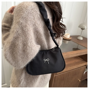 Detalle de bolso bajo el brazo negro con mariposa plateada y correa fruncida elegante