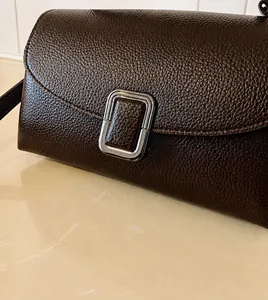 Macro shot of dark brown pebbled leather texture and silver metallic buckle detail