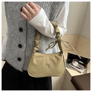 Detalle de bolso mostaza con adorno de lazo metálico y diseño de asa fruncida