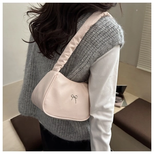 Detail einer rosa Schultertasche mit silberner Schleife über grauem Pullover