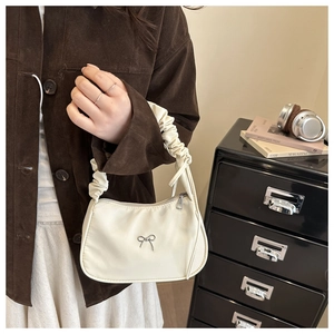 Detalle de bolso de satén blanco crema con mariposa plateada y asa fruncida