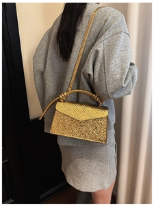 Detail of golden crossbody bag with metallic texture, envelope flap and knot strap
