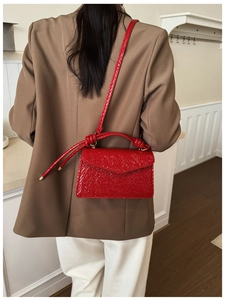 Detail of red crocodile texture handbag featuring unique knotted handle and shoulder strap