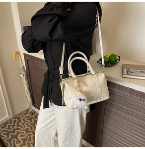 Primer plano del bolso de cuero plisado beige con relieve y colgante de peluche