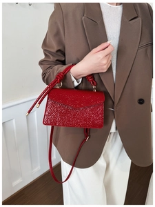 Detail of red textured leather crossbody bag with knot handle and gold hardware