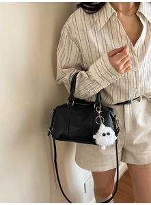 Detail der schwarzen Leder Boston Bag mit weißem Plüsch-Anhänger und Schultergurt