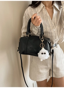 Detail der schwarzen PU-Boston-Tasche mit FASHION AIR PARIS-Gravur und Plüschanhänger