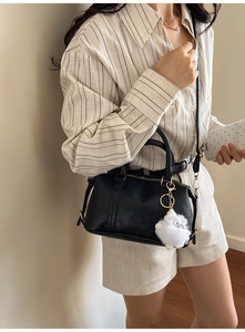 Detail of black Boston bag with leather texture and fluffy white pendant on model