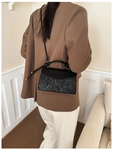 Detail of black textured crossbody bag with glossy flap and metallic shimmer surface