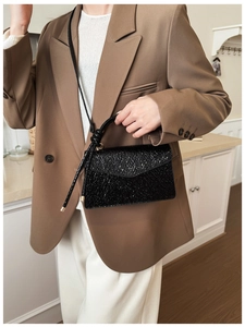 Close-up of model wearing black glossy wrinkled texture handbag with brown suit jacket