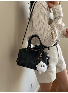Detail der schwarzen Boston-Tasche aus Leder mit Prägung und weißem Monster-Anhänger