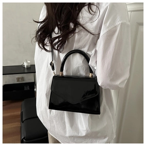 Detail einer glänzenden schwarzen Lackleder-Tasche, die das Modell crossbody trägt