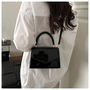 Detail view of shiny black patent leather crossbody bag with gold hardware on a model