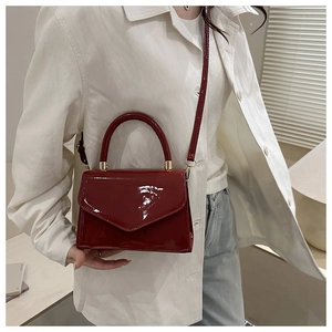 Detail der dunkelroten Lackleder-Handtasche mit goldenen Beschlägen und Gurt