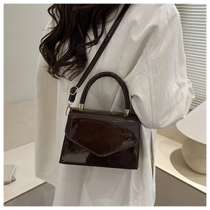Glossy chocolate brown leather handbag shown crossbody on a white oversized blazer