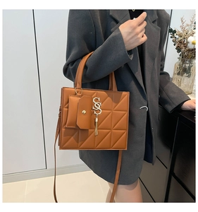 Detail of brown quilted leather bag with gold S-logo, fringe tassel, and mini pouch accessory